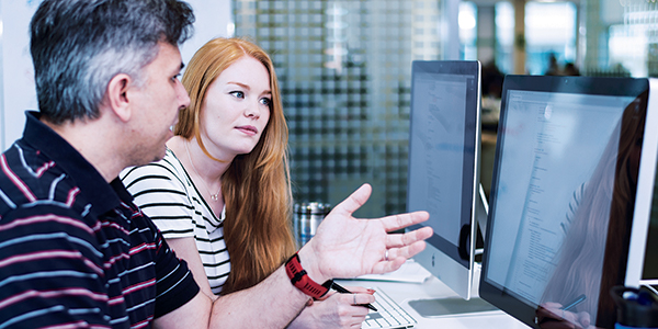 Two co-workers working together while collaborating on work on a computer monitor. 