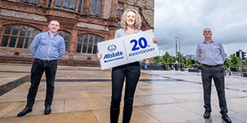 Three ANI employees standing with a sign 20th anniversary. 