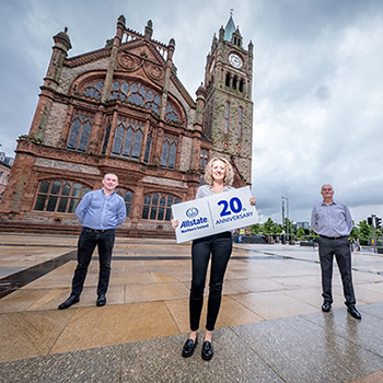 Three ANI employees standing with a sign 20th anniversary. 